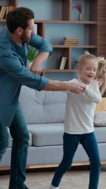 Beyaz aile evde kızlarıyla dans ediyor. El ele zıplıyor, dans ediyor, gülümsüyor, dönüyor, dönüyor, gülüyor, gülüyor, mutlu babayla küçük kız çocuğuyla eğleniyor.