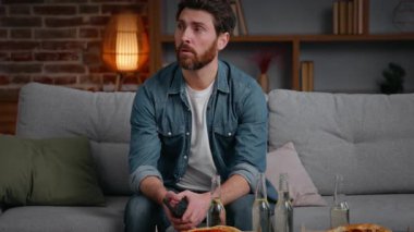 Beyaz, orta yaşlı, hayal kırıklığına uğramış bir adam pizza cipsi ile iptal edildi. Yalnız, yalnız, erkek adam kanepenin üzerinde yalnız, yalnız, kimsesiz doğum gününde yalnızlık karantinada acı çekiyor.