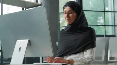 Arap Müslüman, tesettürlü iş kadını ofiste bilgisayar üzerinde çalışıyor. İslamcı iş kadını, internet yazılımı yazıyor. Müşteri gülümsemesi ile sohbet ediyor.
