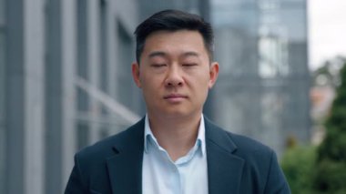 Şehirdeki yakın plan portre sakin Asyalı ciddi iş adamı orta yaşlı iş adamı kendinden emin Çinli işveren Koreli erkek profesyonel kameraya bakıyor.