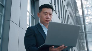 Asyalı iş adamı Koreli orta yaşlı iş adamı laptopuyla şehirde erkek Japon işvereni kablosuz taşınabilir bilgisayar yazarak uzaktan kumandalı bir işte çalışıyor.