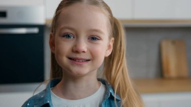 Kafkasyalı mutlu küçük bir kızın yakın portresi. Neşeli bir şekilde gülümsüyor. Mutfak kameralarına bakıyor.
