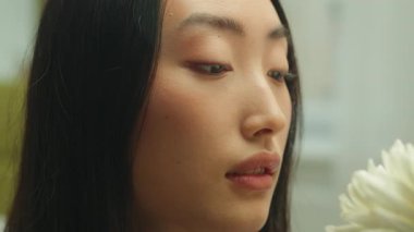 Kapalı portre. Çiçek kokan Asyalı kadın. Elinde beyaz kasımpatı olan aroma bitkisi.