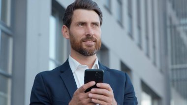 Beyaz, orta yaşlı iş adamı şehir merkezindeki erkek işadamında modern alet bağımlılığı kullanarak cep telefonuyla iş adamı arıyor. Dışarıdaki aletle akıllı telefon girişimciliği yapıyor.