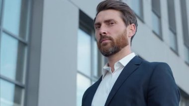 Kafkasyalı yetişkin iş adamı şehirde kameraya bakıp gülümseyen başarılı, orta yaşlı, erkek, yönetici, profesyonel, güler yüzlü, ofis binası yakınında mutlu bir girişimci.