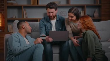 Heyecanlı dört arkadaş internetten alışveriş yapıyor kanepeye ev yemeği siparişi veriyorlar. Çeşitli erkekler, kredi kartı internet ödemelerini laptopta yapıyorlar. Başarı parasını geri alıyorlar.