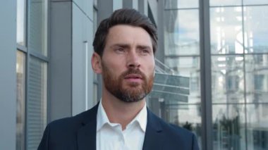 Orta yaşlı, düşünceli, Kafkasyalı bir işadamı ofis binasının yakınındaki şehirde yürüyor cam duvarın yanındaki şirkete gidiyor ve erkek yöneticinin işe gitmeyi düşündüğünü söylüyor.