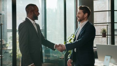 İki etnik çeşitlilikte iş adamı şirket ofisinde tokalaşıyor, konuşuyor, çeşitli beyaz iş adamları el sıkışıyor, gülümseyen Afrikalı Amerikalı erkeğe hoş geldin diyor.