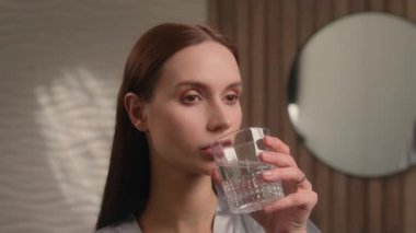 Sabah banyo sıhhatinde gülümseyen bir kadın. Elinde cam hidrasyon dengesi olan sağlıklı beyaz bir kadın. Vitamin alışkanlığı.