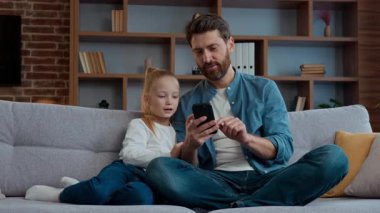 Evde mutlu bir beyaz aile babası ve kızı cep telefonuyla komik videolar izliyorlar. Akıllı telefonlu çocuk ve bekar babayla yemek sipariş ediyorlar. Modern cihaz ebeveyn kontrolü kullanıyorlar.