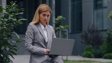 Odaklanmış Kafkasyalı orta yaşlı iş kadını şehirde dizüstü bilgisayar yazıyor yetişkin iş kadını kadın bilgisayar işçisi şehir dışında şirket hizmetlerinde çalışıyor bilgisayar işçisi olarak çalışıyor.