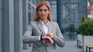 Ciddi derecede dakik Kafkasyalı yetişkin bir iş kadını kol saatini işaret ederek kameraman iş kadınına bakıyor şehir merkezindeki kadın işverenin saat başı portresini kontrol ediyor.
