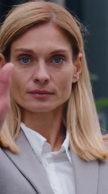 Ciddi bir beyaz iş kadını elinde avuç içi jesti ile kameraya bakıyor ve şehir merkezindeki iş kadınını reddettiğini gösteriyor. Yönetici gösteri yasağı işareti. Mesafeyi koru işareti.