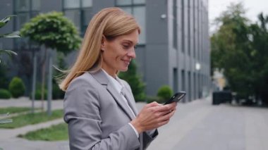 Kafkasyalı mutlu orta yaşlı iş kadını telefonuyla sohbet ediyor şehir merkezinde cep telefonlu bir iş kadını ve cep telefonuyla e-posta yazarken gülümsüyor.