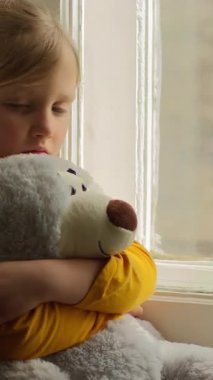 Stresli küçük kız çocuğu pencereye bakıyor oyuncak ayıya sarılıyor evde yalnızlık çekiyor evde yalnızlık çekiyor kederli bir çocukluk çocuğu evde yalnız başına zihinsel sağlık psikolojisini benimsiyor.