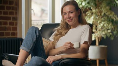 Kafkasyalı rahat bir kadın sabah kahvesinin tadını çıkarıyor aromalı içecek kokuyor ev sahibi bayan iş kadını dinleniyor evde oturup kameraya bakıyor çay molası veriyor ve evde huzur içinde dinleniyor.