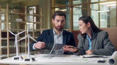 Rüzgâr türbini güneş paneli yatırımcılarını sunan çok ırklı iş mühendisleri ekoloji enerjisi yenilikçiliğiyle tanışan Koreli kadın Kafkas erkeği sürdürülebilir teknoloji işbirliği çalışma alanı ofis doğası