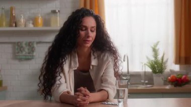 İspanyol asıllı beyaz bir kadın evinde acı çekiyor. İlaç içiyor. Cam, baş ağrısı, semptom, sağlık, kadın, evde ilaç içiyor.