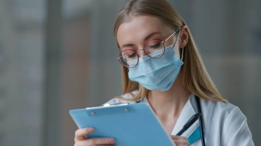 Kafkasyalı maske takan doktor kadın hemşire hastane kliniğinde düşünceli bir kadının yazdığını düşünüyor. Teşhis kovid19 çalışma laboratuarı. Yüksek kalite 4k