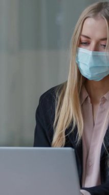 Sağlık maskeli, beyaz iş kadını ofis bilgisayarında çalışıyor hasta kız iş kadını internette sohbet ediyor. Şirket salgınının önlenmesi Coronavirus Sağlık Hizmetleri 'nde bilgisayar kullanıyor.