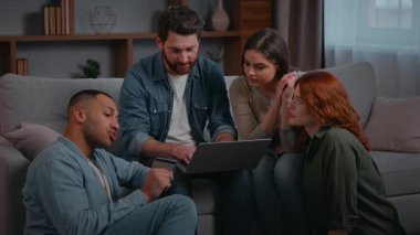 Birden fazla etnik gruptan dört arkadaş kanepe üzerinde dizüstü bilgisayar arıyorlar. Çok ırklı etnik gruplar. Erkekler ev partilerinde toplanıp online proje hakkında konuşuyorlar.