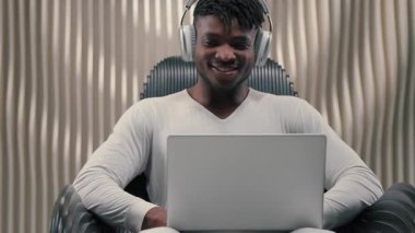 Afro-Amerikalı bir adam, gelecekteki stüdyo erkeğinin bilgisayarında fütürizm siber uzay teknolojisi kullanarak dizüstü bilgisayar yazarken yenilikçi stüdyoda kulaklık takarak sanal oyun oynarken kaygısız gülümsüyor.