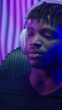 Kablosuz kulaklıklı sakin Afro-Amerikalı adam müzik dinliyor. Fütürist karanlık neon mekanında müzik dinliyor. Sandalyede dans ediyor.