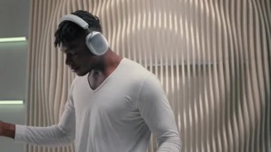 Dans dinleyen, kulaklıklı Afro-Amerikan bir adam müzik sesinden, kaliteli, modern kulaklıklardan hoşlanır. Fütürizm stüdyo dansında erkek, fütüristik beyaz uzay trendi kulübünde dans ediyor.