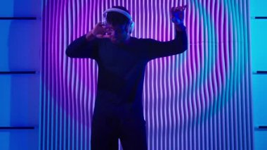 Genç, Afro-Amerikan kulaklıklı, neon fütüristik kulüpte enerjik müzik dinleyen, kulaklıklı, neşeli, erkek kulaklıklı, mutlu, duygusal enerjili dans fütürizmi partisinden memnun bir adam.