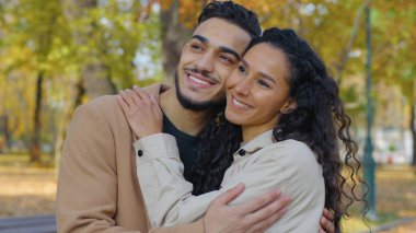 Yakın planda mutlu İspanyol çift gülen dişlek, sonbahar parkında kucaklaşan, sarılan Arap aile kucaklaşmasını seven açık havada sarılan, güler yüzlü, evli, kadın ve sonbaharda düşen adama bakan.