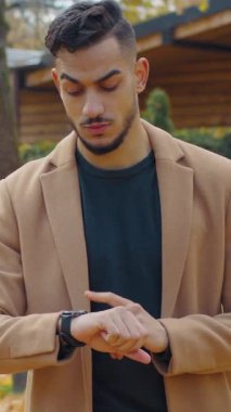 Sonbahar parkında endişeli İspanyol bir adam kol saatine bakarak buluşmayı bekliyor. Hayal kırıklığına uğramış saati kontrol ediyor. Sonbahar sezonunda dışarıda dikilen üzgün erkek.