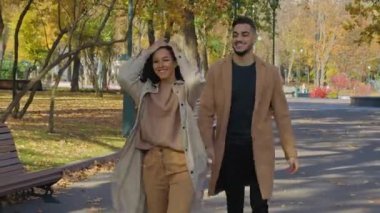 Mutlu İspanyol çift, güz parkında el ele tutuşup gülerek gülerek neşeli, çok ırklı aile yürüyüşleri yaparak gülerek gülerek, Arap bir adamla birlikte beyaz bir kadının keyfini çıkarıyor.