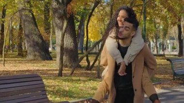 Sonbahar parkındaki mutlu İspanyol çift, sırtında bir kadınla uçuyormuş gibi yapıyor, kız ellerini açıyor, gülüyor, hafta sonu randevularından bahsediyor, eğleniyor, sonbahar sezonunun tadını çıkarıyor.