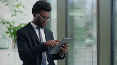 Odaklanmış Afro-Amerikan işadamı dijital tablet kullanarak internet üzerinde çalışan kablosuz bilgisayar teknolojisi iş adamı erkek işvereni ile veri analizi yapıyor.