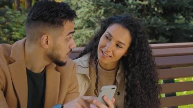 Sonbahar parkında birlikte cep telefonu kullanan çok ırklı Latin kökenli neşeli çift ekranda yemek siparişi vermeyi seçiyor.