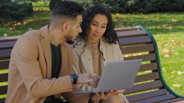 Mutlu İspanyol çift, sonbahar parkında dizüstü bilgisayarla kazanıyor. Yedek kulübesinde oturan Arap erkek, beyaz kadın, çok ırklı evli kız ve bilgisayarlı adam zafer için iddiaya giriyor.