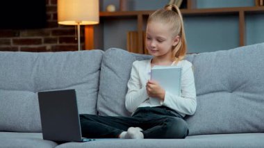 Kafkasyalı mutlu kız çocuğu. Kanepe üzerinde dizüstü bilgisayarla yazı yazıyor. Uzaktan eğitim alıyor, ev ödevlerini yapıyor.