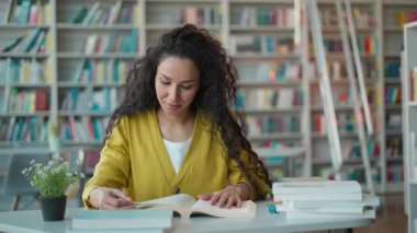 Latin bayan öğrenci kütüphanede kitap okurken gülümseyen İspanyol kadın öğrenci hayrete düştü. Hobi okuyucu, üniversite üniversite sınavlarına hazırlanıyor. Harika bir ders kitabı eğitimi.