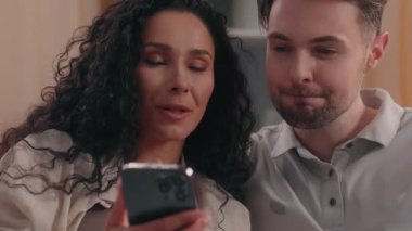 Çok ırklı, beyaz, İspanyol bir kadın cep telefonu kullanıyor. Akıllı telefonlu, erkek, erkek, erkek, erkek, kocası. Latin, kız, kadın, kız arkadaşı, evde tatil planları yapıyor.