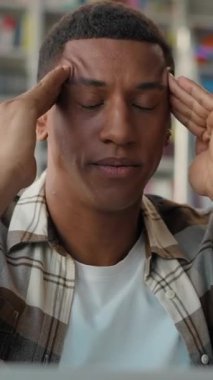 Stresli Afrikalı Amerikalı erkek öğrenci kütüphanede masaj yapıyor baş ağrısı çekiyor gözleri kapalı migren hastası yorgun erkek sınav baskısı öğreniyor yorgunluk mücadele motivasyon sorunu