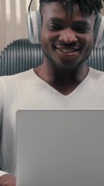 Afro-Amerikalı bir adam, gelecekteki stüdyo erkeğinin bilgisayarında fütürizm siber uzay teknolojisi kullanarak dizüstü bilgisayar yazarken yenilikçi stüdyoda kulaklık takarak sanal oyun oynarken kaygısız gülümsüyor.