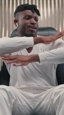 Afro-Amerikalı adam kulaklıkla müzik dinliyor, dans ediyor, koltukta dinleniyor, dans ediyor, el sallıyor, dans ediyor, kulaklık takıyor, fütürizm uygulamasında şarkı dinliyor.