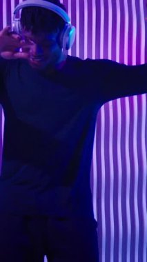 Genç, Afro-Amerikan kulaklıklı, neon fütüristik kulüpte enerjik müzik dinleyen, kulaklıklı, neşeli, erkek kulaklıklı, mutlu, duygusal enerjili dans fütürizmi partisinden memnun bir adam.