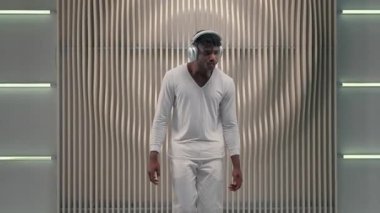 Afrikalı Amerikalı erkek dans modern kablosuz kulaklıklarla müzik dinlemeyi sever. Fütürist erkek kulaklık takıyor. Fütürizm odasında dans ediyor.