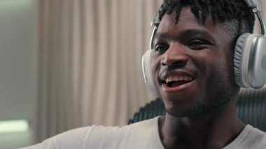 Kablosuz kulaklıklı aktif duygusal Afrikalı Amerikalı adam heyecanlı bir şekilde müzik dinliyor modern kulaklıklarda kaliteli ses teknolojisi fütüristik stüdyoda gülümseyen erkek adam dans ediyor, eğlenceli şarkı söylüyor.