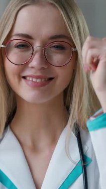 Kafkasyalı doktor, klinikte gülümseyen jest misali baş parmağını göstererek hastanede tedavi aşısı öneren neşeli, mutlu kadın tıp kızına bakıyor.