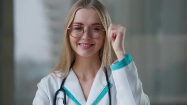 Kafkasyalı doktor, klinikte gülümseyen jest misali baş parmağını göstererek hastanede tedavi aşısı öneren neşeli, mutlu kadın tıp kızına bakıyor.