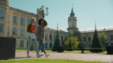 Kampüs dışında iki çok ırklı kadın birlikte ders arası veriyor. Öğrenciler, kızlar, çeşitli arkadaş grupları. Beyaz Afrikalı, yürüyen kadınlar, açık hava lisesi üniversitesinde konuşuyorlar.