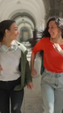 Üniversite koridorunda gülerek koşan iki mutlu kız öğrenci aktif sınıfa koşuyor gülümseyen kızlar, gülümseyen bayan arkadaşlar Latin Latin Latin çok ırklı kadınlar, derslere geç kalıyorlar.