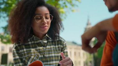 Mutlu gülümseyen Afrikalı Amerikalı iki öğrenci kampüs kadınlarının önünde gülüyor komik iletişim kuruyor arkadaşlık adamı ev ödevi kitapçığını tartışıyor kadın erkek öğreniyor